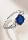 A Queensmith cushion sapphire engagement ring with pear shape diamond side stones, and a plain platinum band