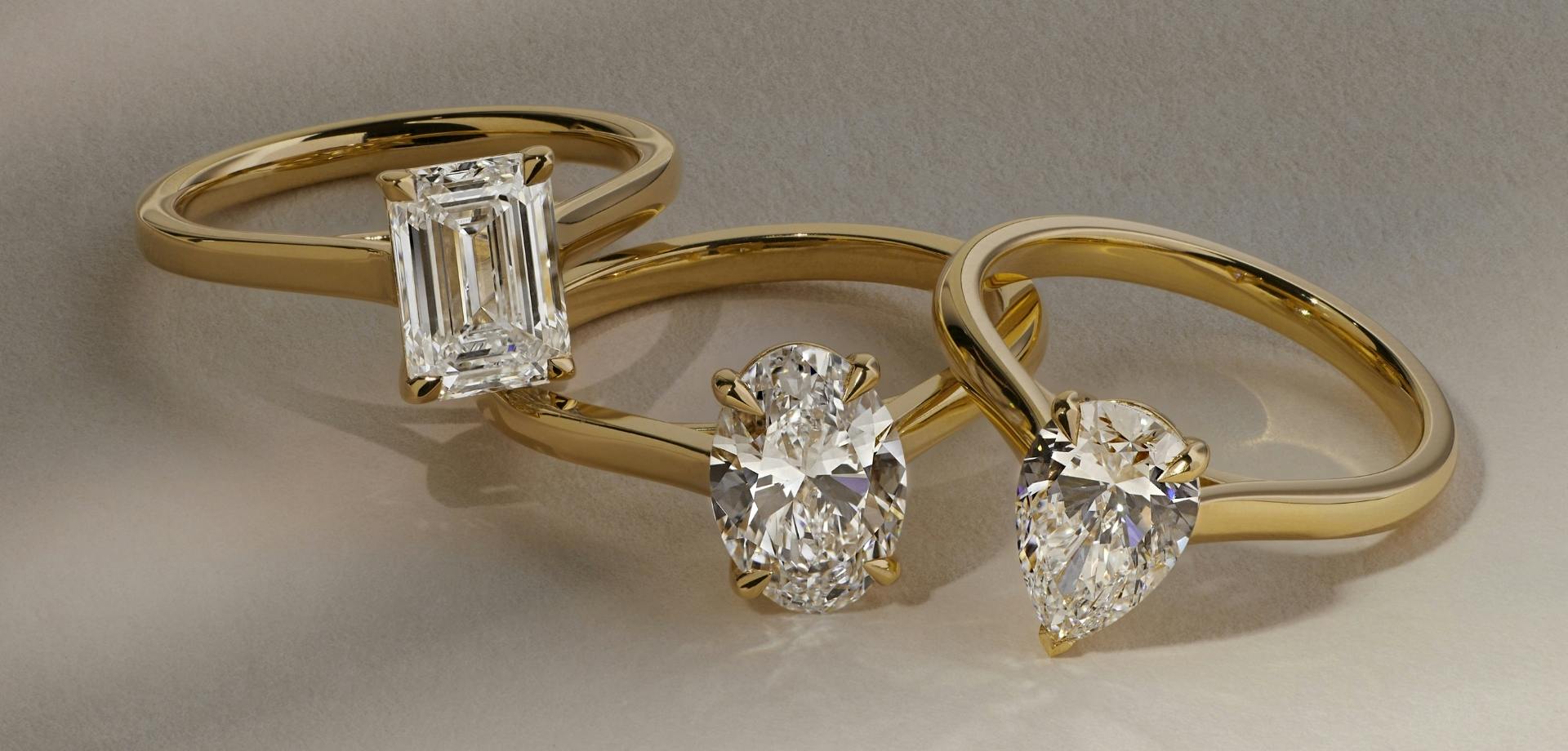 A close-up front-view image of three diamond engagement rings in yellow gold, layered over one another in a chain formation.