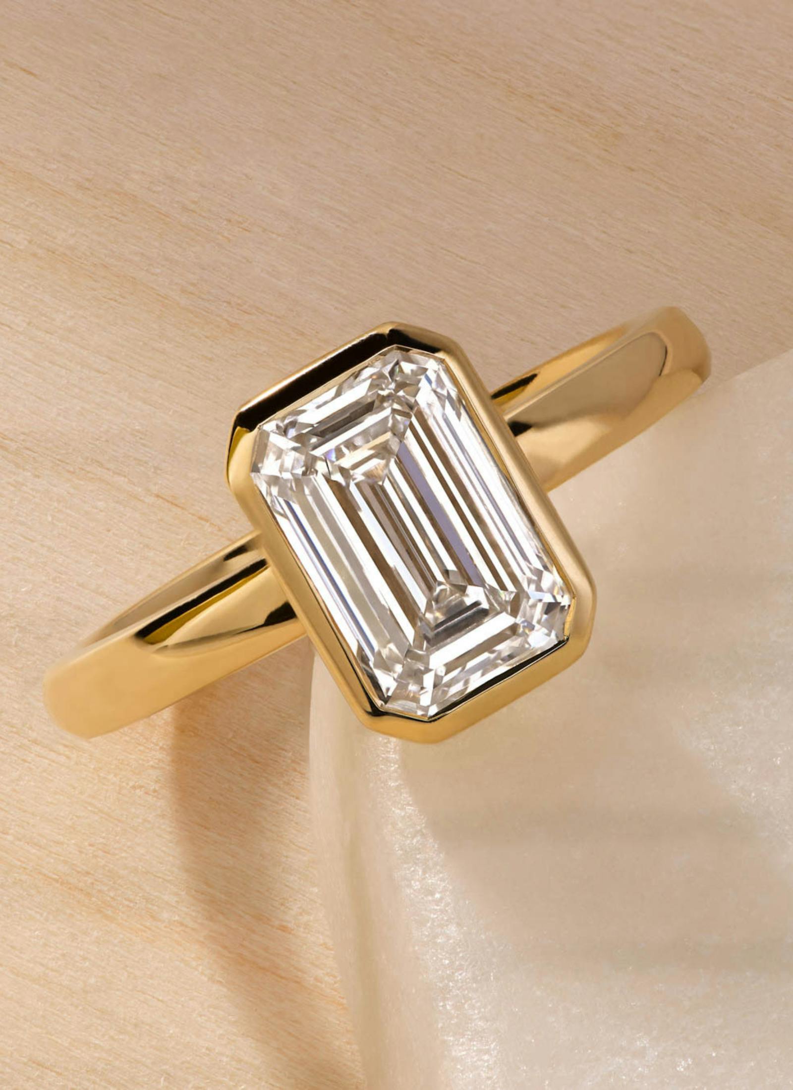 Custom-designed emerald cut engagement ring in a sleek rubover setting, crafted in yellow gold for a bold, modern look with maximum diamond security.