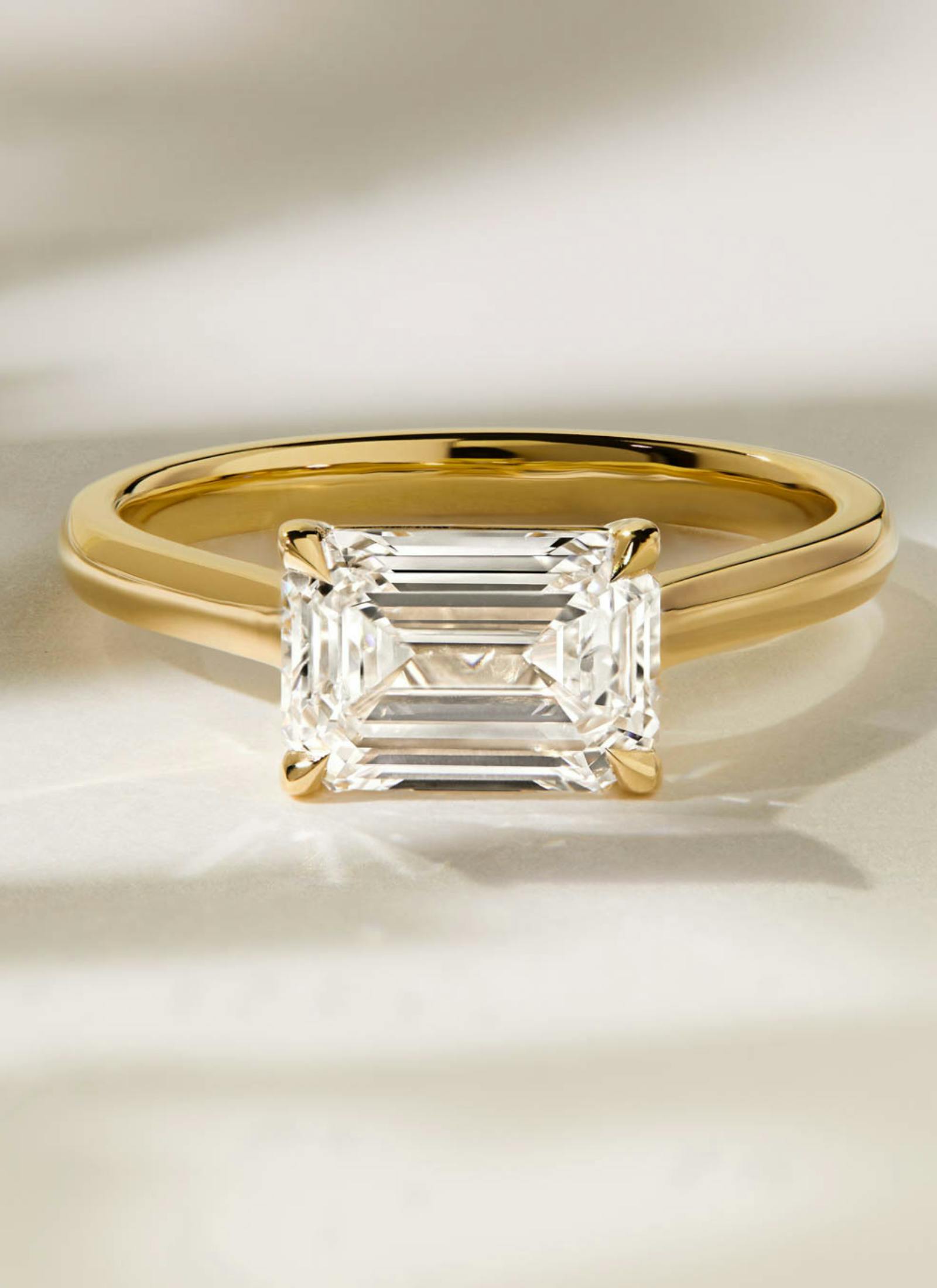 Bespoke four-claw emerald cut solitaire engagement ring in yellow gold, designed with a minimalist band to showcase the diamond’s clean geometry and step-cut brilliance.