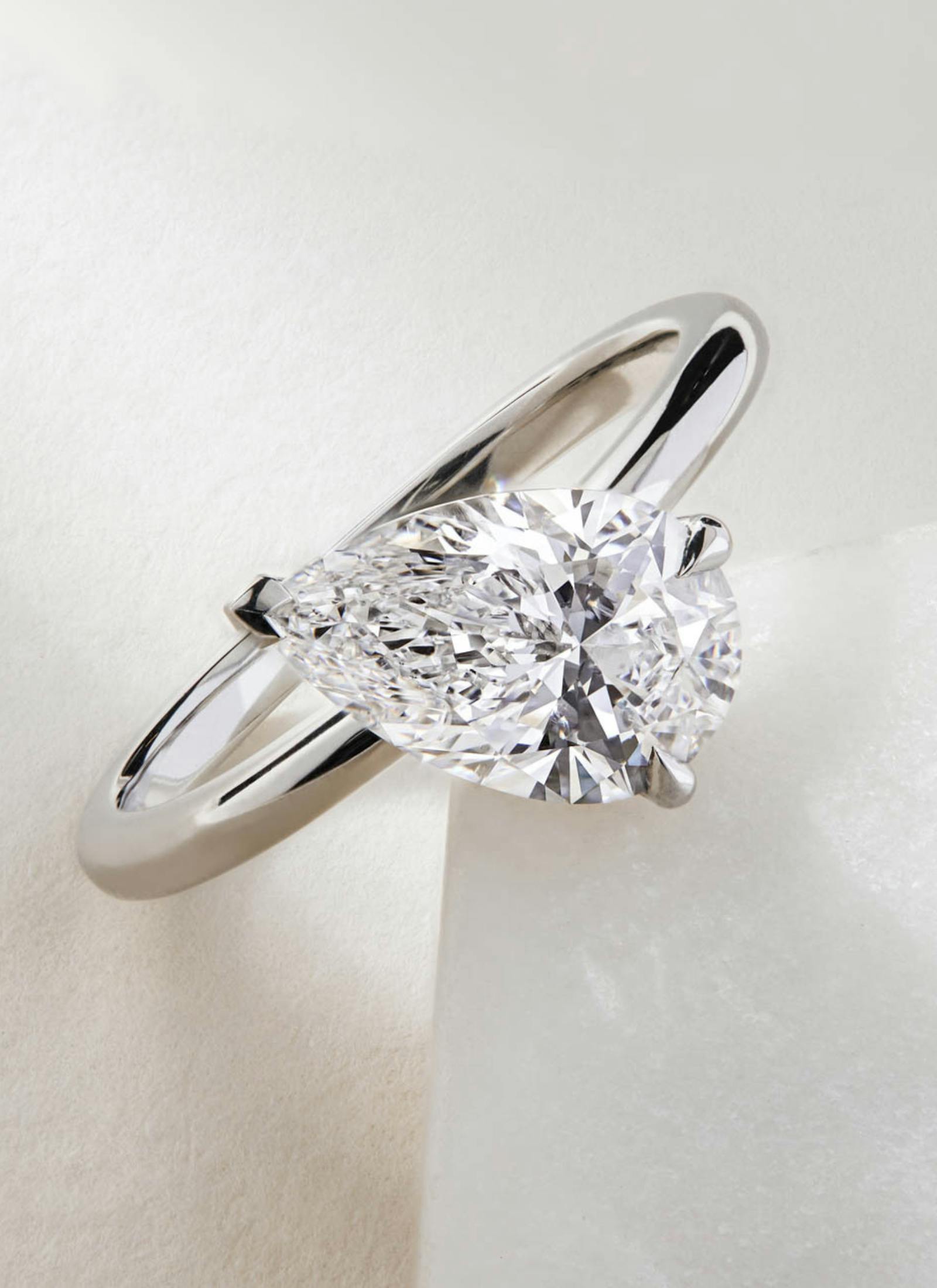 Custom platinum engagement ring with a tilted pear cut diamond, designed in a sleek, minimalist setting to emphasise the stone’s elegant shape and brilliance.