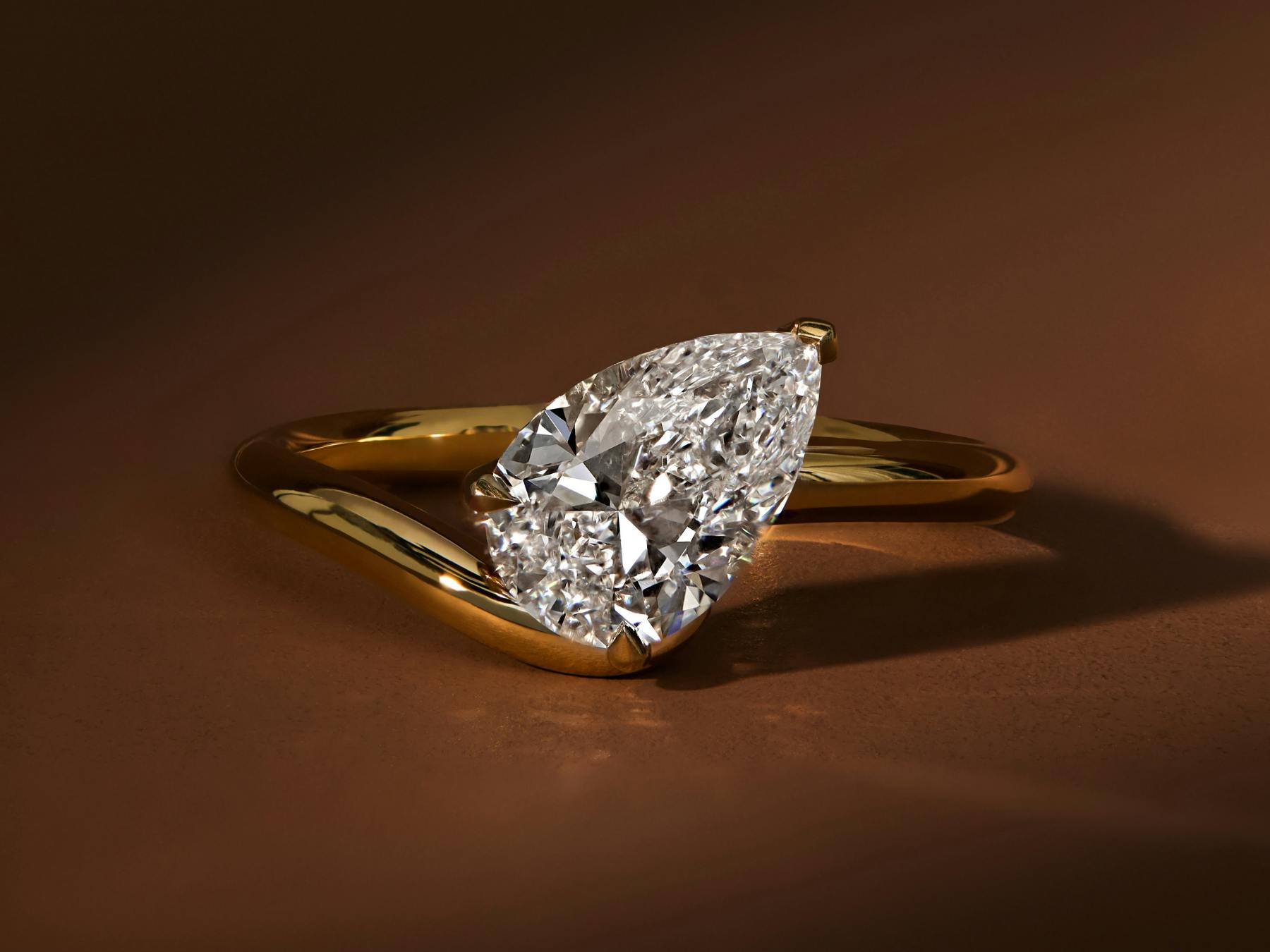 Yellow gold wave contour band engagement ring with tilted pear diamond.
