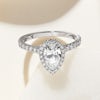 A lab grown pear diamond, platinum halo ring with diamonds along the band and around the diamond, on a plain background