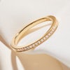A thin, simple pavé diamond wedding ring in yellow gold on top of white fabric