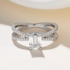 A modern lab grown emerald cut diamond engagement ring with a double diamond band that crosses over to meet the diamond