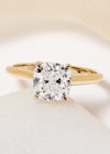 a large, 2ct cushion cushion shape yellow gold solitaire ring, on a plain background with soft shadows