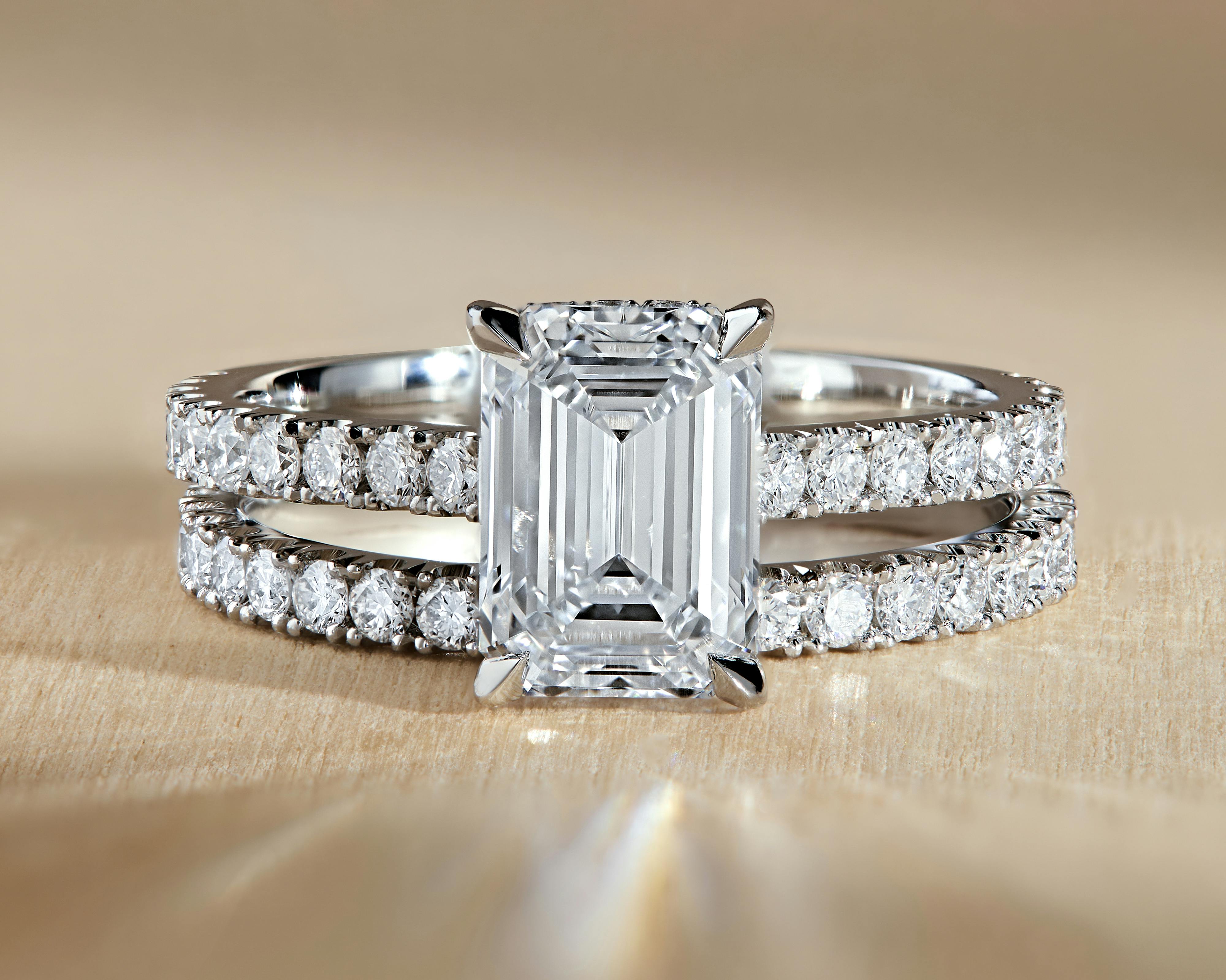 A bardot scallop emerald cut platinum engagement ring on a wood grain table.