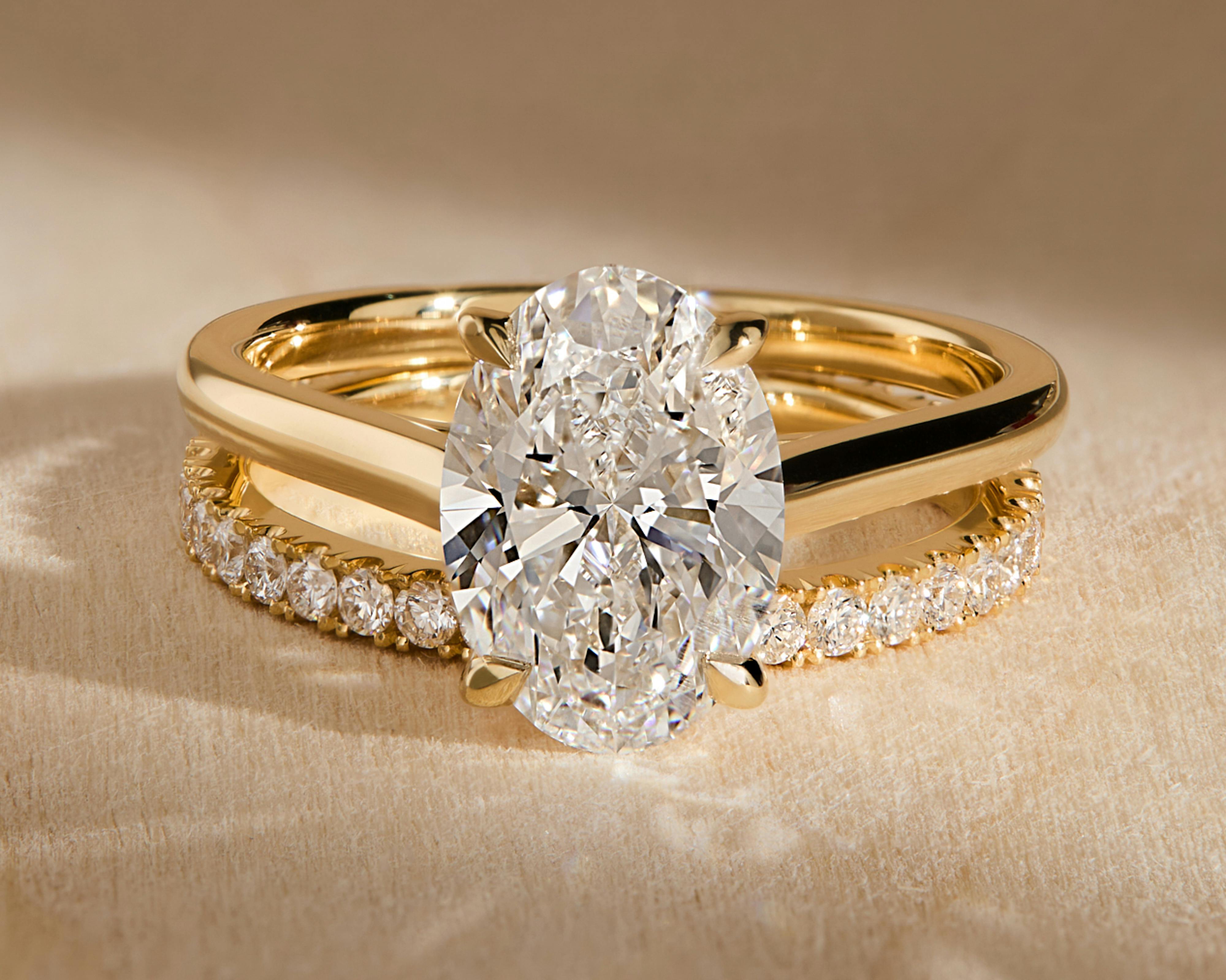 A bardot oval yellow gold engagement ring on a wood grain table.