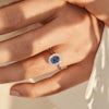 Close up of woman's hand wear an oval sapphire engagement ring with diamond halo by Queensmith jewellers