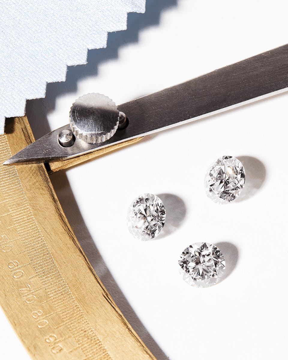 Three loose diamonds on a table with a diamond measuring tool and pale blue polishing cloth