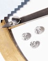 Three loose diamonds on a table with a diamond measuring tool and pale blue polishing cloth