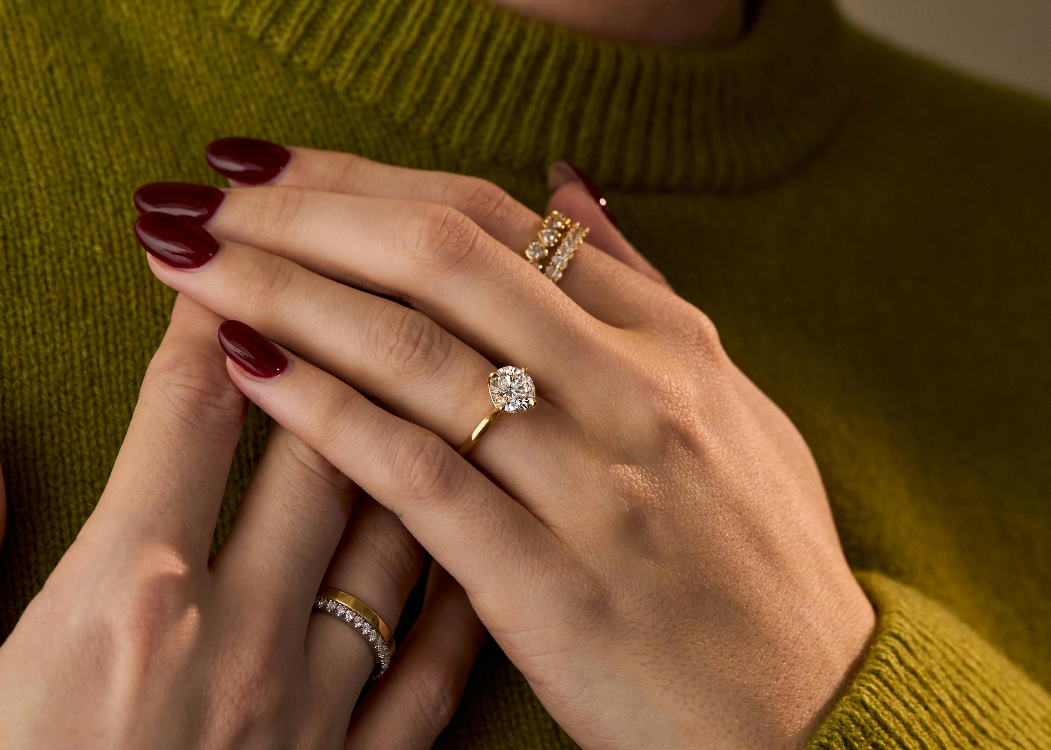 A close-up shot of a woman's manicured hand, showcasing a comfortable-fitting round brilliant diamond ring in yellow gold.