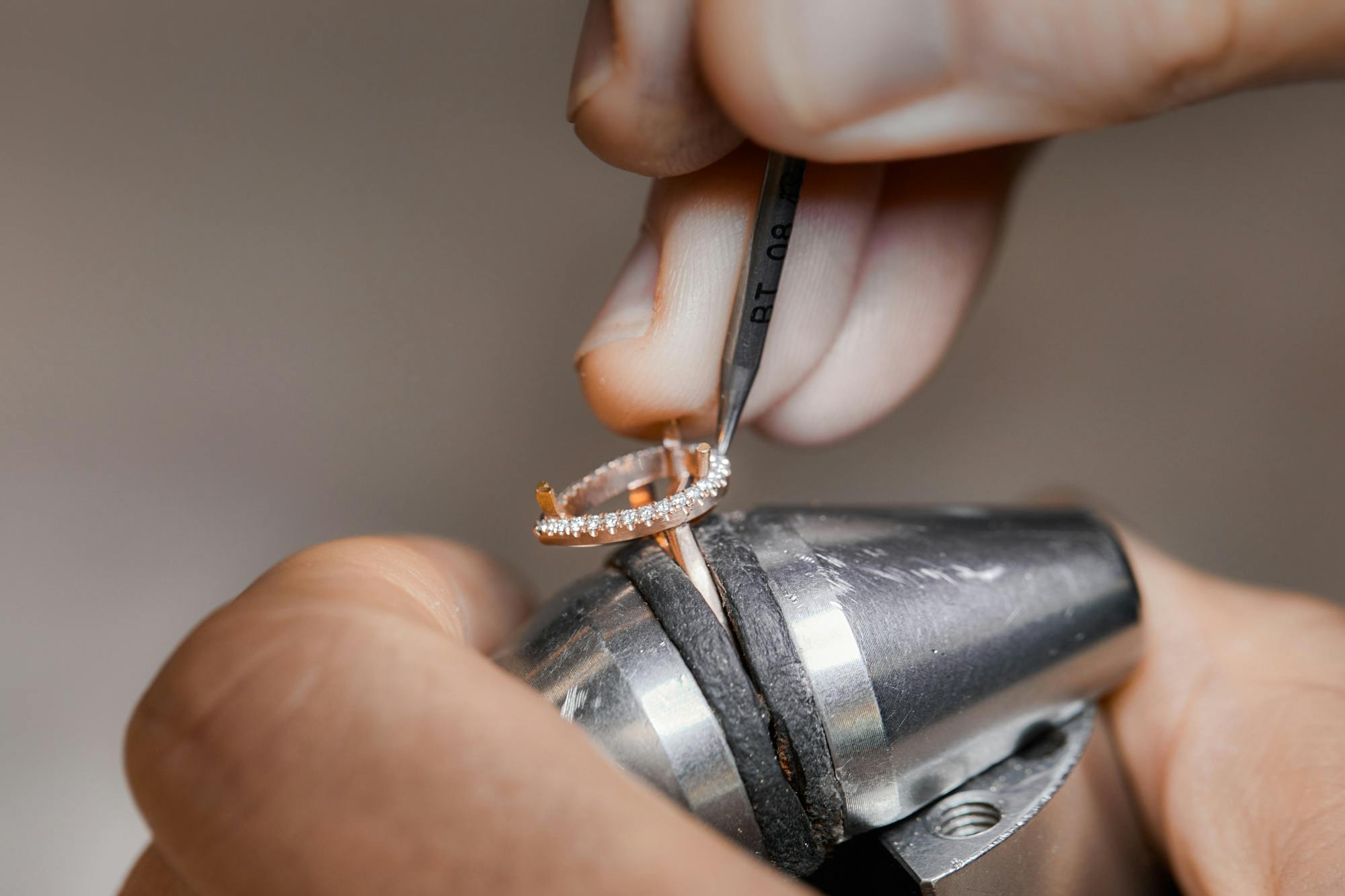 Close-up image of a setter's hands as they carefully position melee diamonds in a halo formation around a pear-shaped diamond, set into the ring band.
