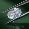 Oval lab grown diamond held by tweezers against green background.