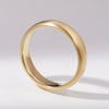 A plain, matte yellow gold wedding ring standing up on its side on a white background