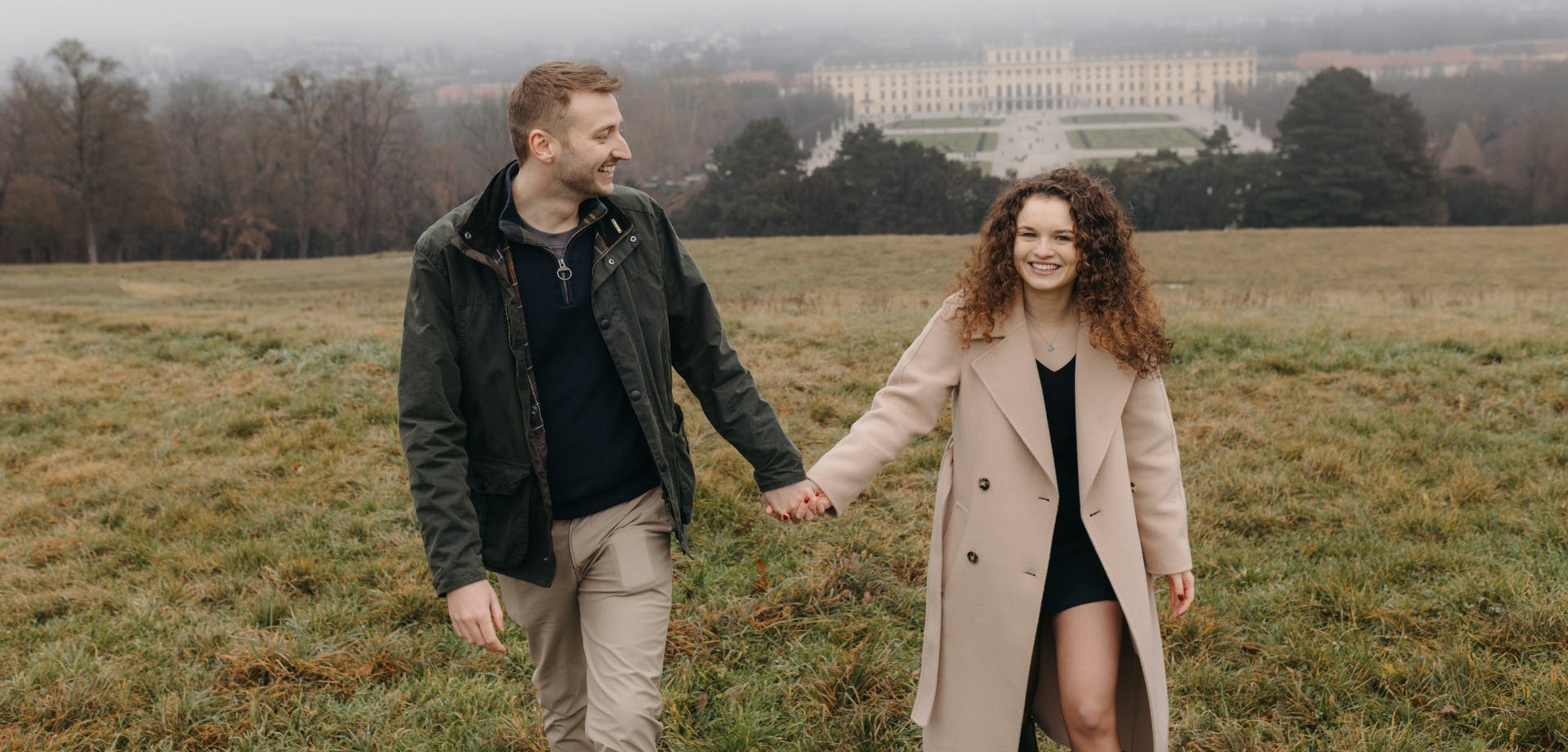 Couple holding hands during a proposal at Schönbrunn Palace in Vienna, with sweeping city views behind them.
