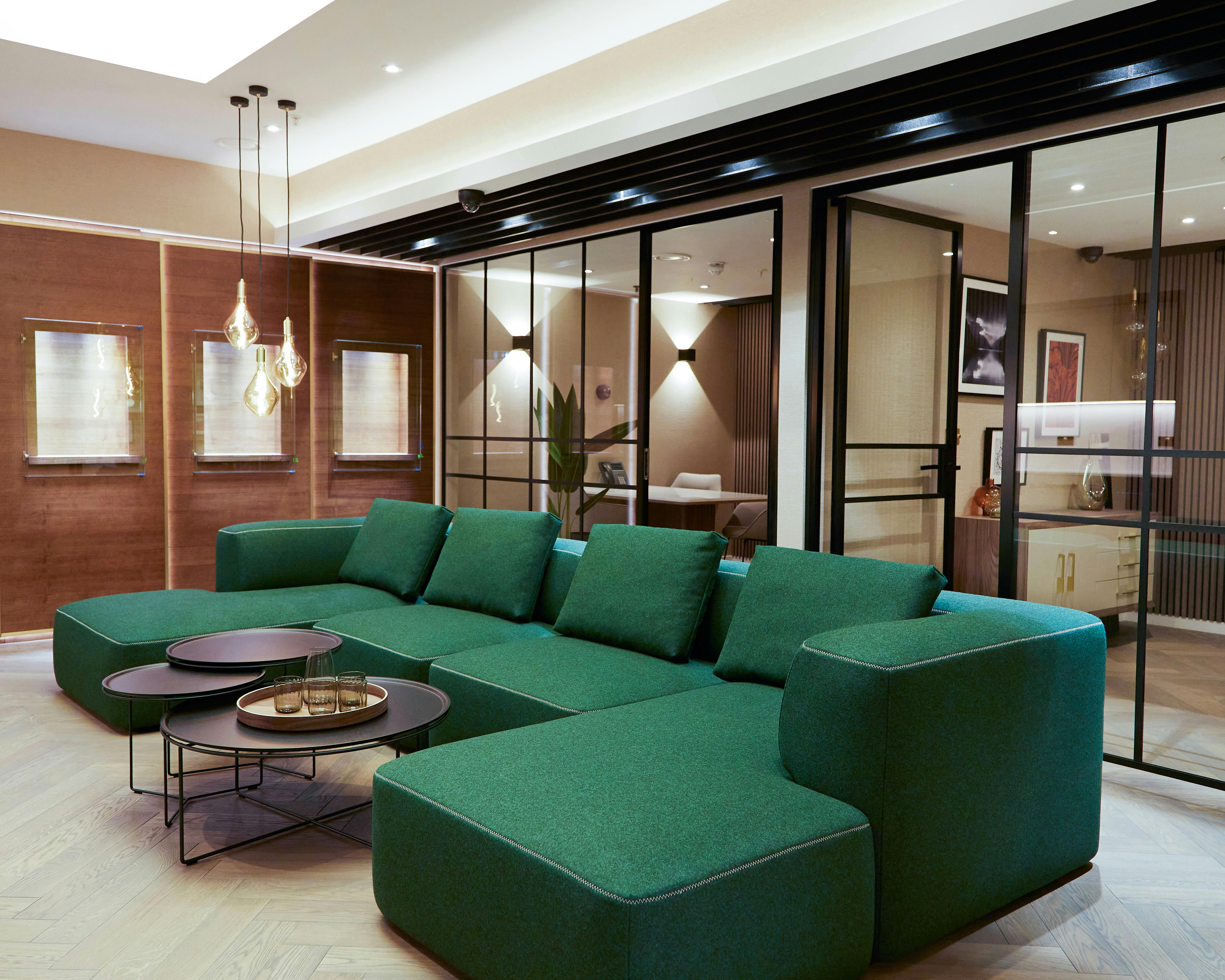 The client waiting area at Queensmith, tastefully decorated with modern lighting and furnishing, and a comfy green sofa. The ambience is calm and serene.
