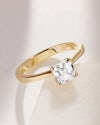 Small asscher shape solitaire diamond ring yellow gold, simply resting on the tile with a plain background, framed by shadows