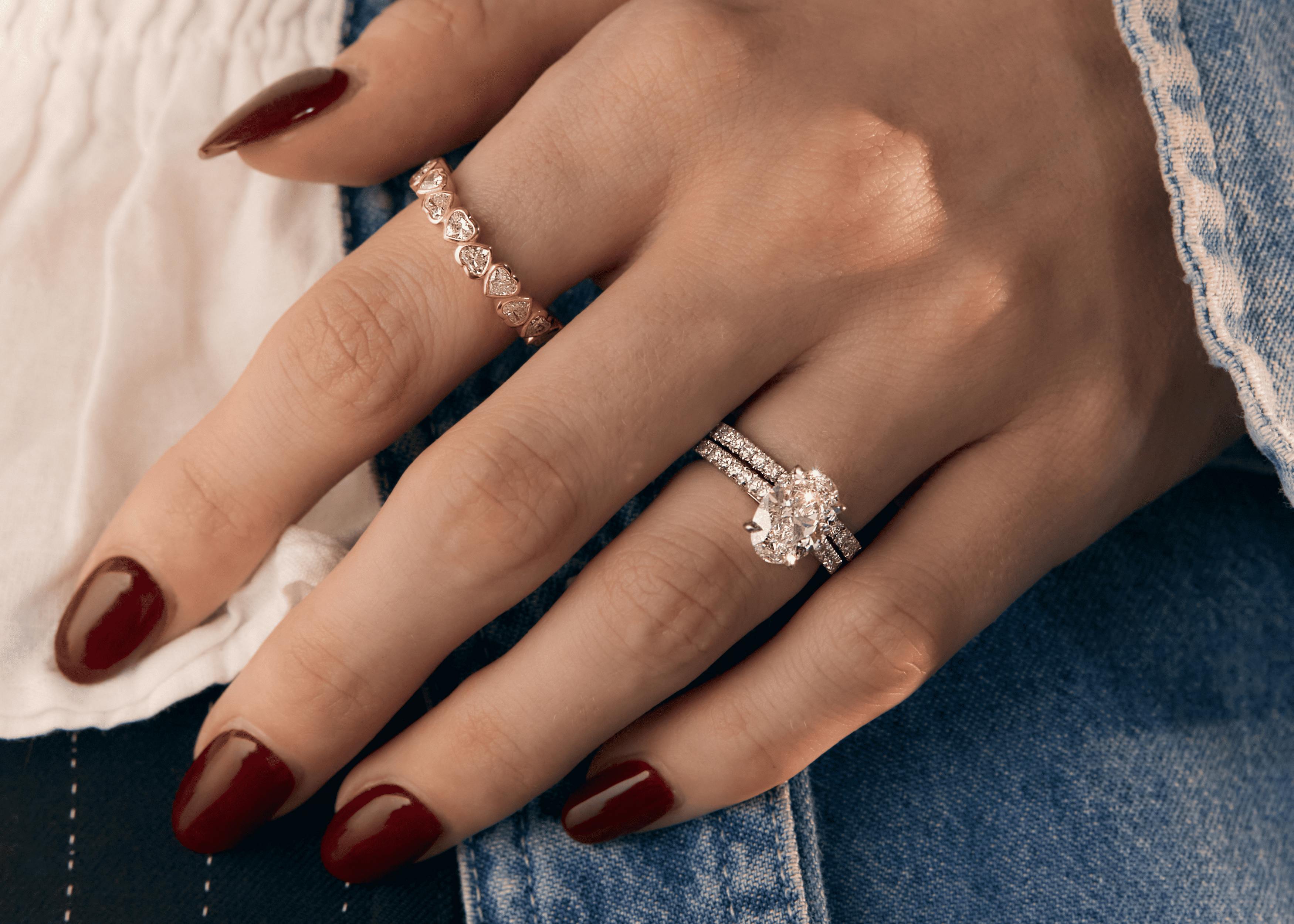 Ring stacking across multiple fingers with gold diamond bands and oval cut diamond engagement ring.