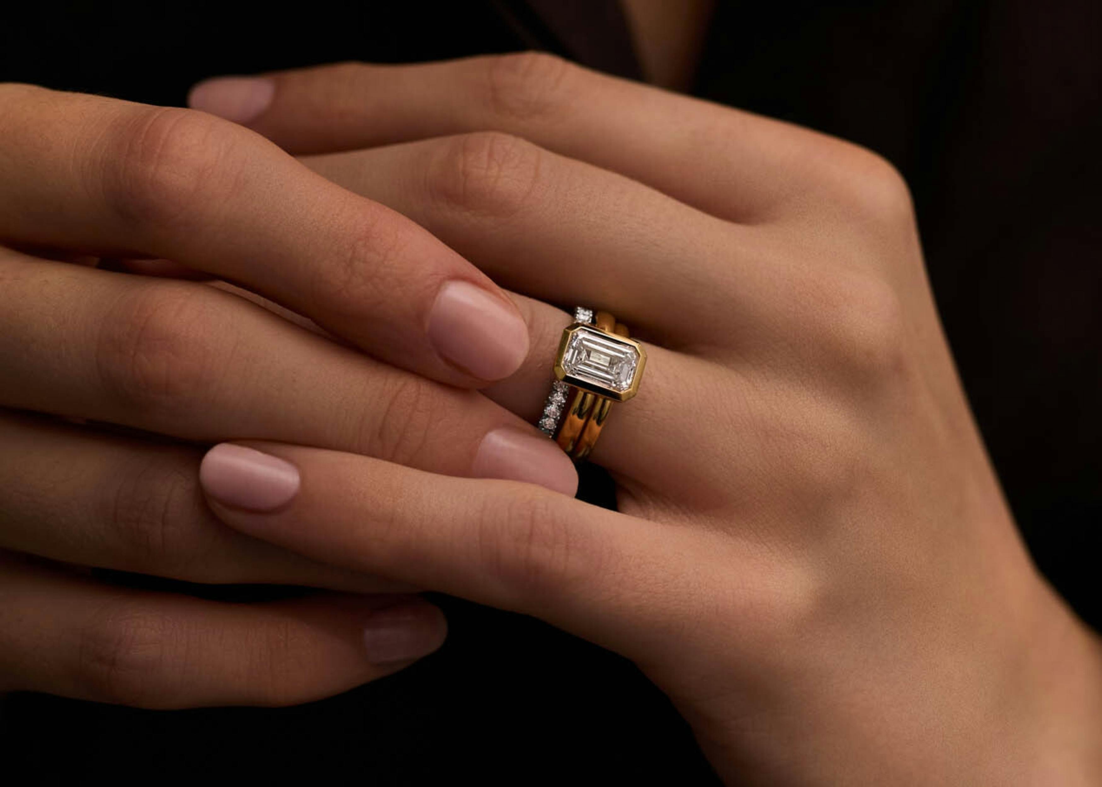 Close-up shot of a woman's hands as she adjusts her diamond wedding band and flush fit emerald cut engagement ring in yellow gold.