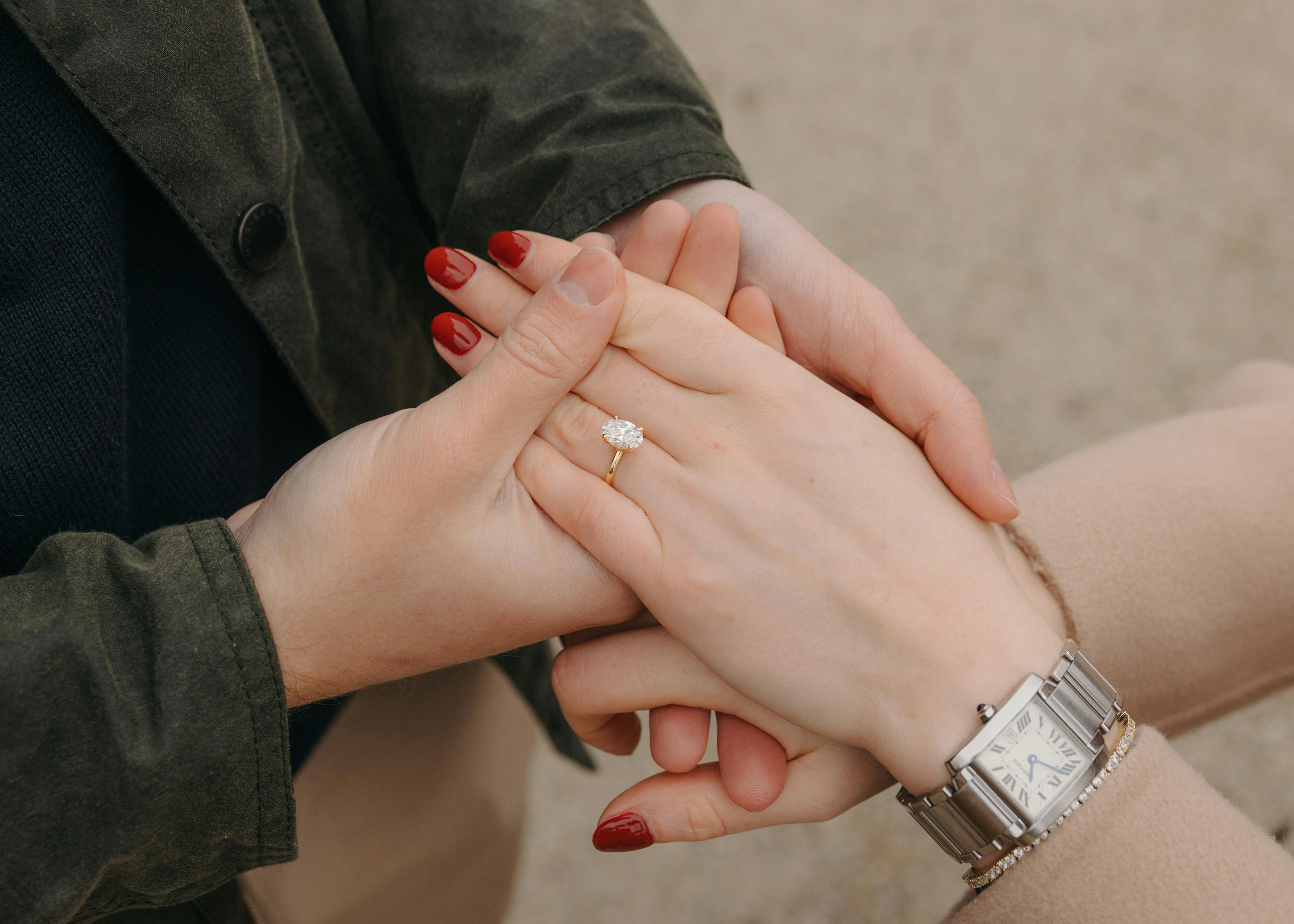 Detailed close-up of a bespoke oval diamond solitaire engagement ring in 18k yellow gold on Ella’s hand.