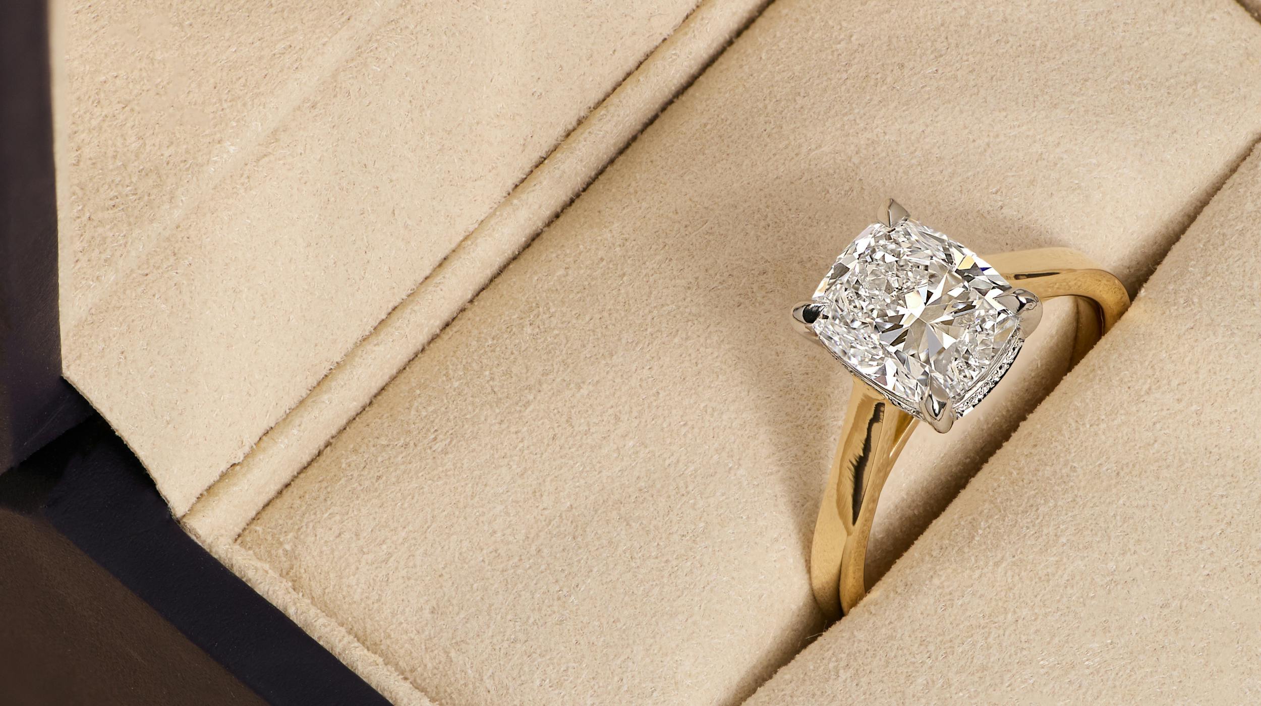 Cushion cut diamond engagement ring with yellow gold band in ring box.