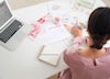 Wedding planner sat at a desk with laptop, notebook, calendar and photos.