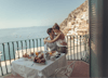 Newlyweds embrace on a balcony overlooking the sea.
