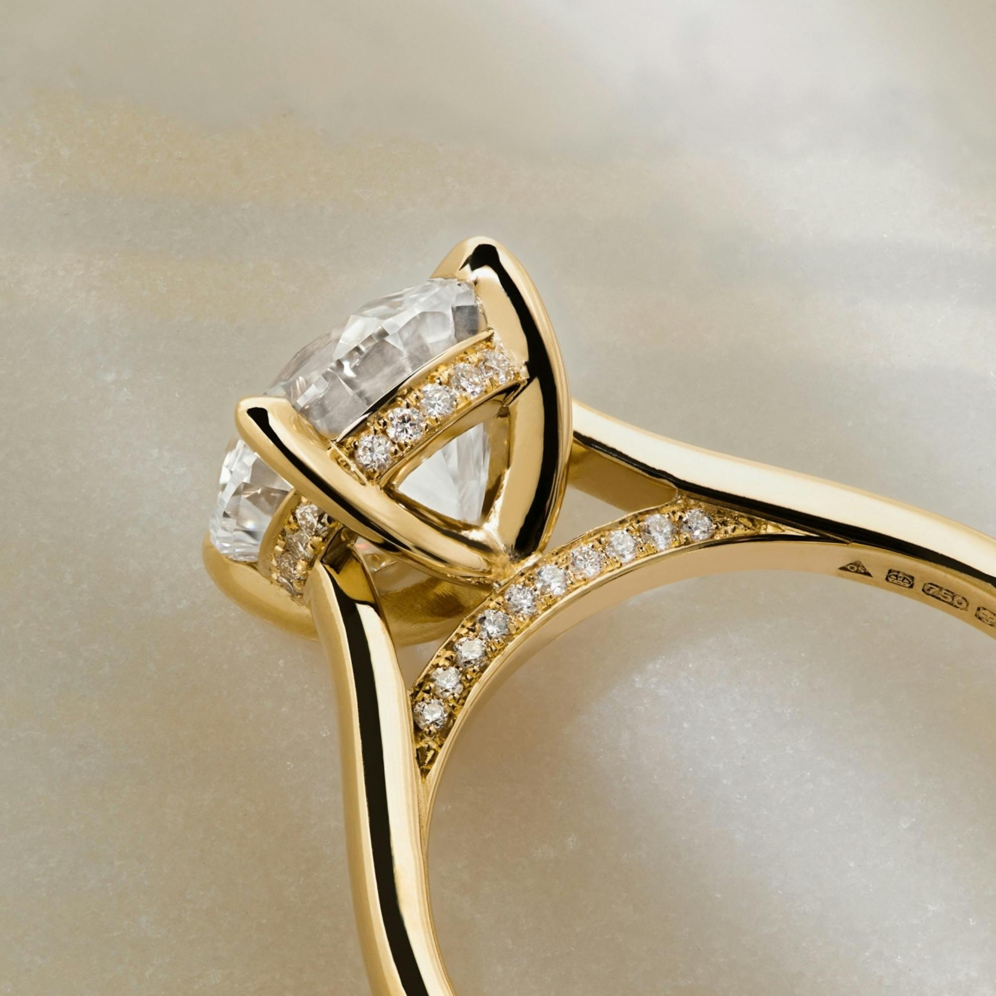 A close-up, aerial-view of a yellow gold Bardot solitaire diamond engagement ring made by Queensmith.