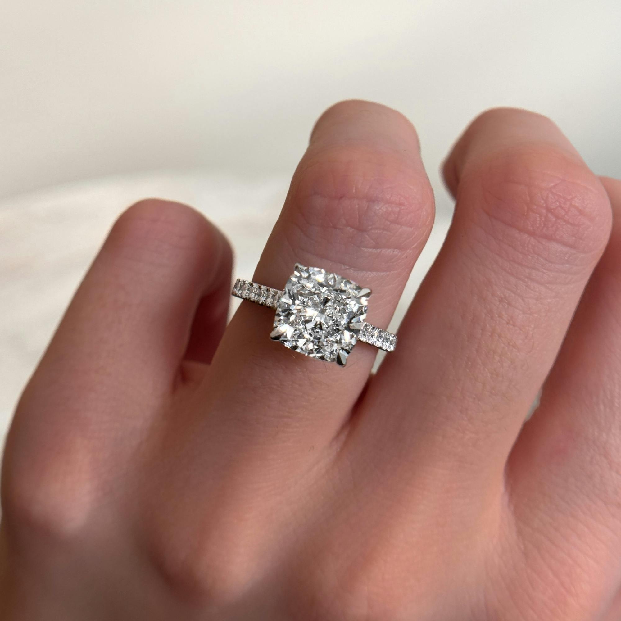 Close-up, self-taken image of the picture taker's hand fashioning a cushion cut diamond engagement ring in platinum.