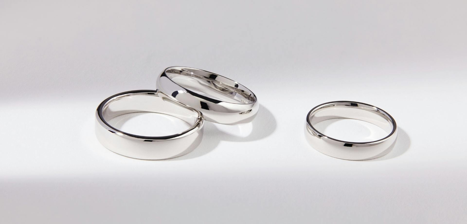 Side-view shot of three white gold wedding bands on a white, lit-up background.