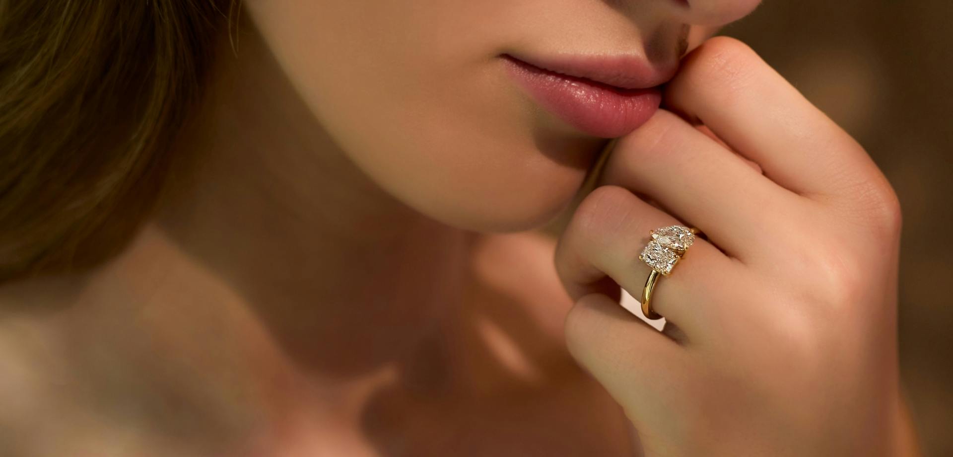 Close-up shot of a woman holding her hand to her face, showcasing a toi et moi diamond ring in yellow gold.