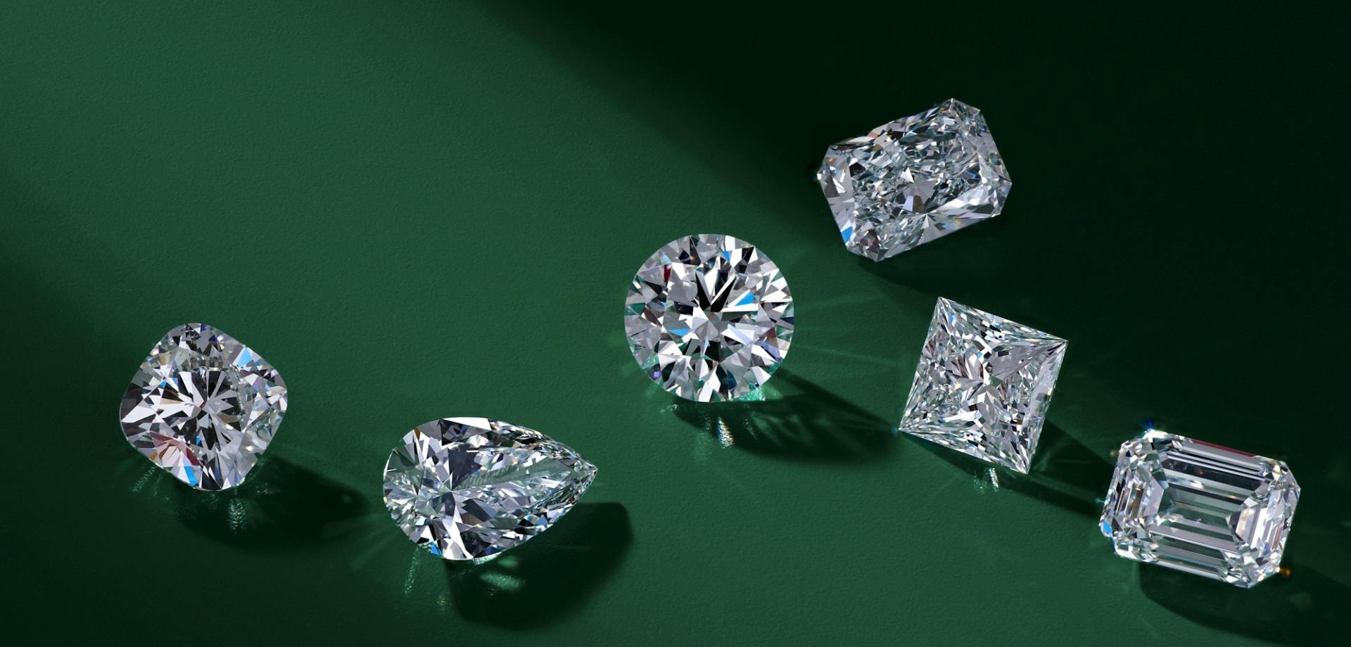 A side-view shot of a loose lab grown diamond flat lay in a variety of shapes, set on a rich emerald green background.
