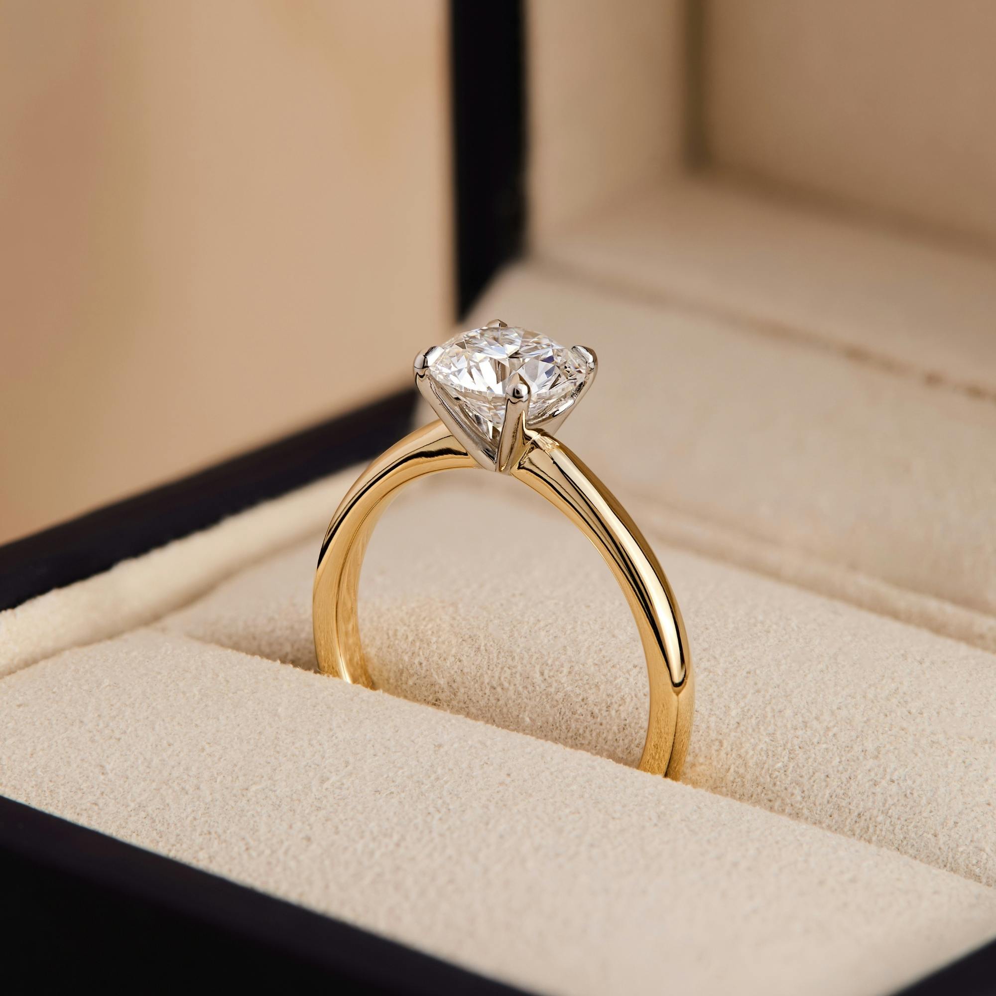 Side-view image of a low-profile solitaire diamond engagement ring in yellow gold nestled within an open ring box.