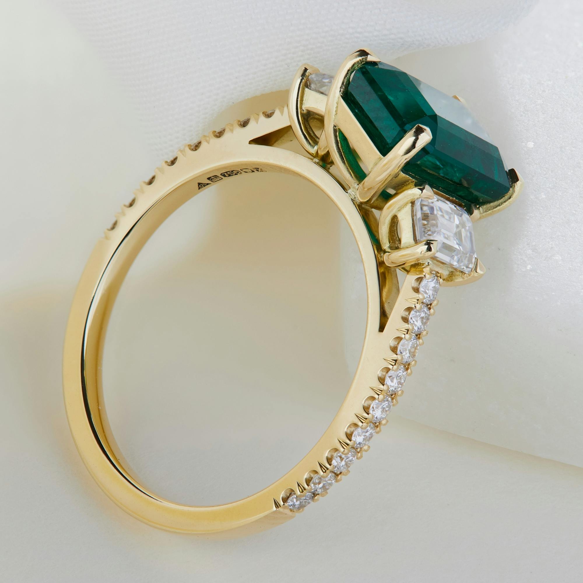 An side-aerial view image of a bespoke, non-wedfit emerald Leigh trilogy engagement ring.