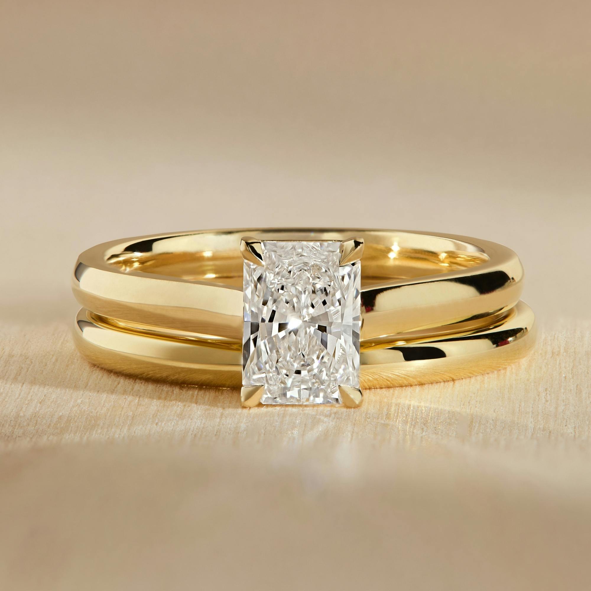 Close-up, face-on image of a radiant cut diamond engagement ring in yellow gold positioned flush against a matching yellow gold wedding band.