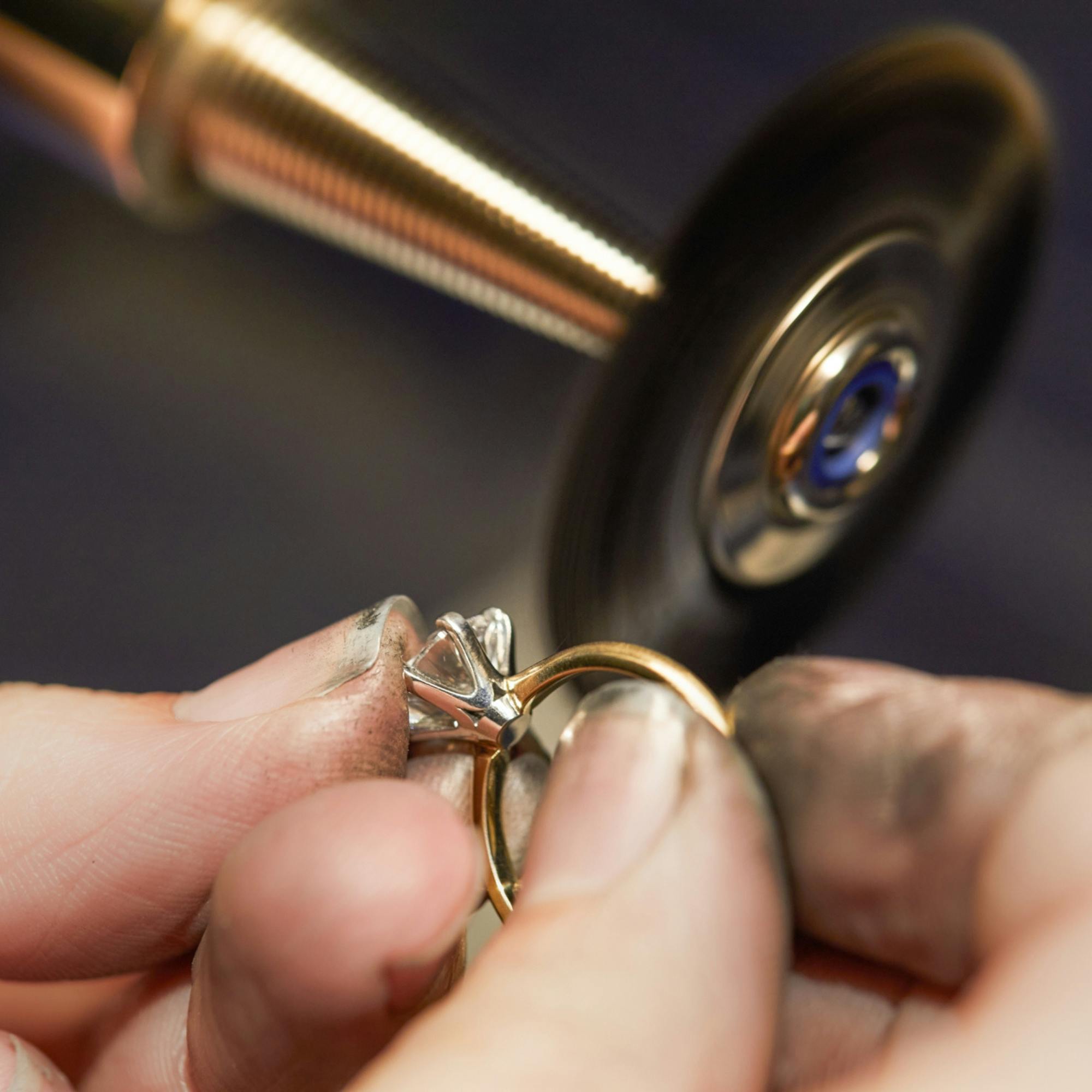 Elevated close-up side view shot of a person polishing a white gold ring - the second step in the rhodium replating process.