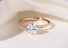 Simple round diamond 6 claw rose gold solitaire engagement ring, on a simply plain white background with a small big of soft, white fabric and soft shadows out of focus
