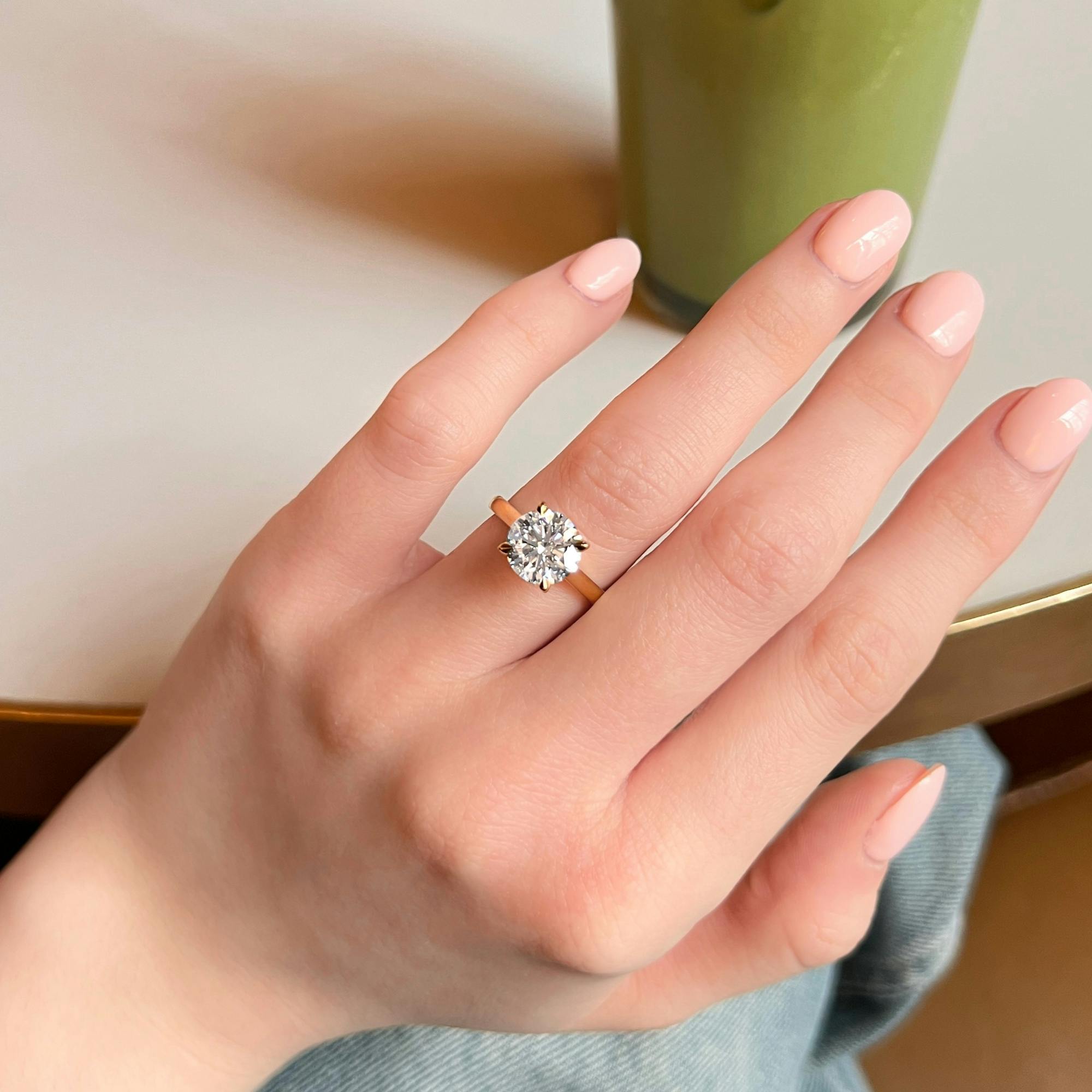 A self-taken image of the picture taker's left hand fashioning a round brilliant diamond engagement ring.