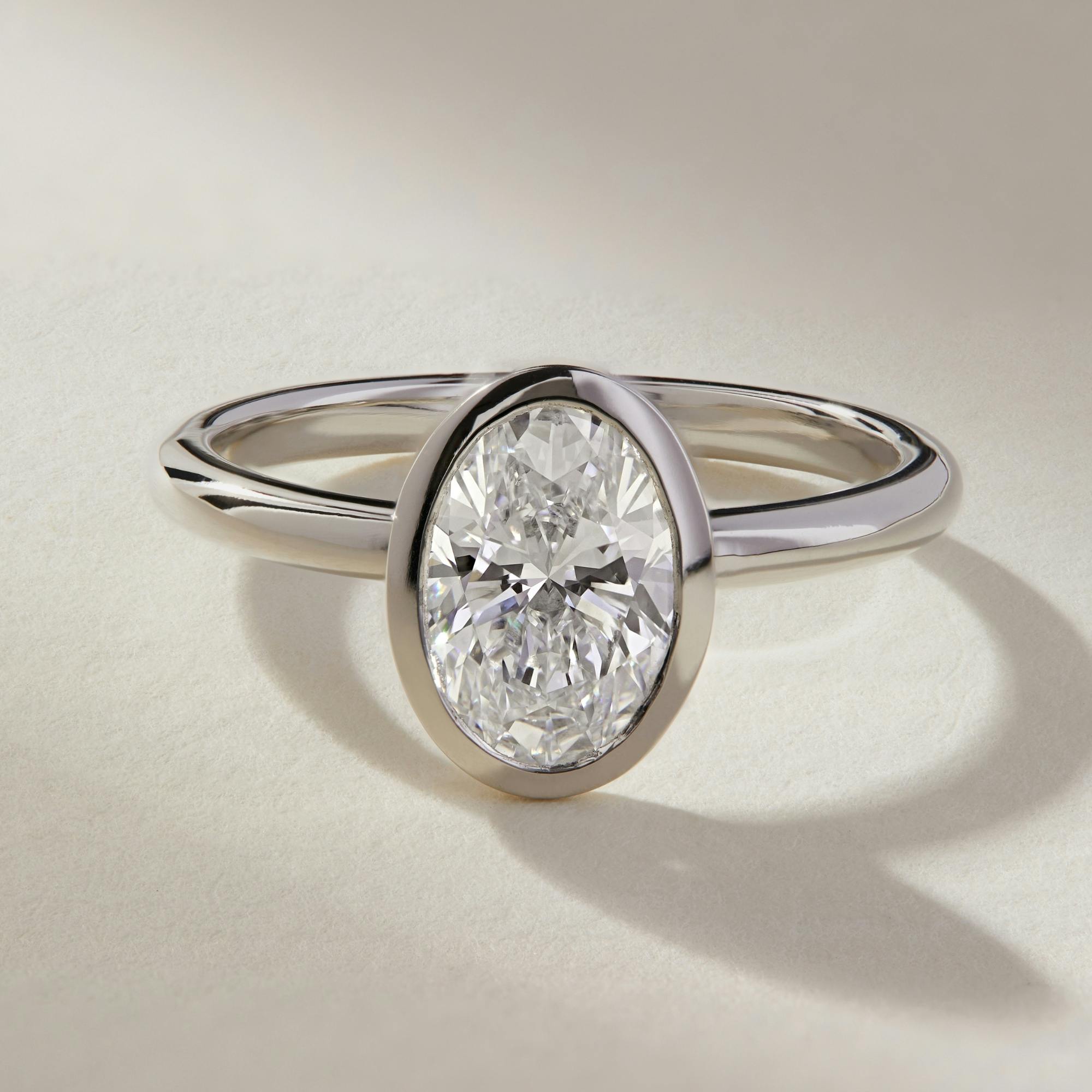 A close-up, front-view shot of an oval diamond engagement ring in platinum with a rubover - also known as a bezel - setting for extra protection.