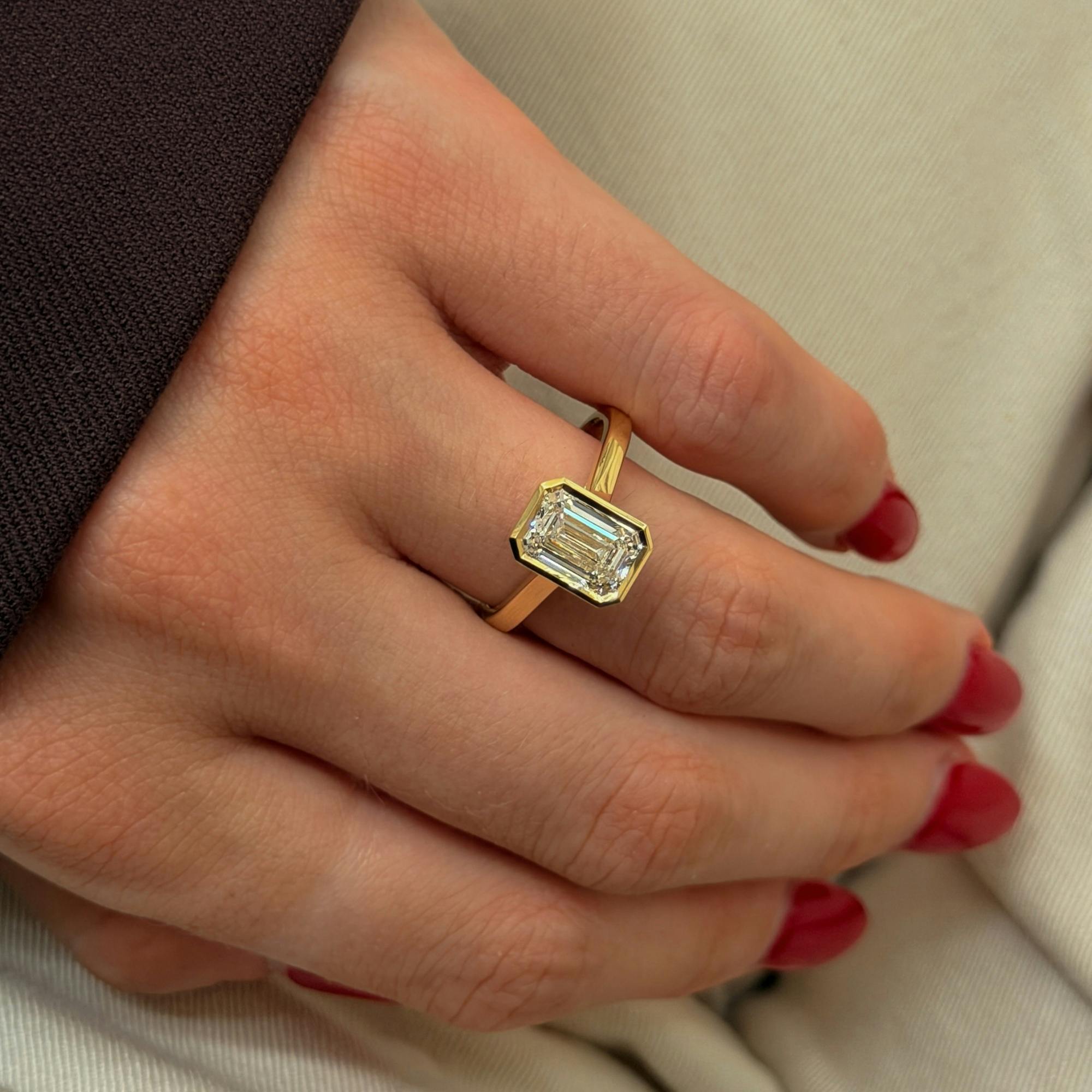 An aerial-view image of a manicured hand fashioning a 2.09ct emerald bespoke diamond engagement ring with a rubover setting.