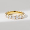 A thick, yellow gold diamond wedding ring set in a shared prong style ona  plain background
