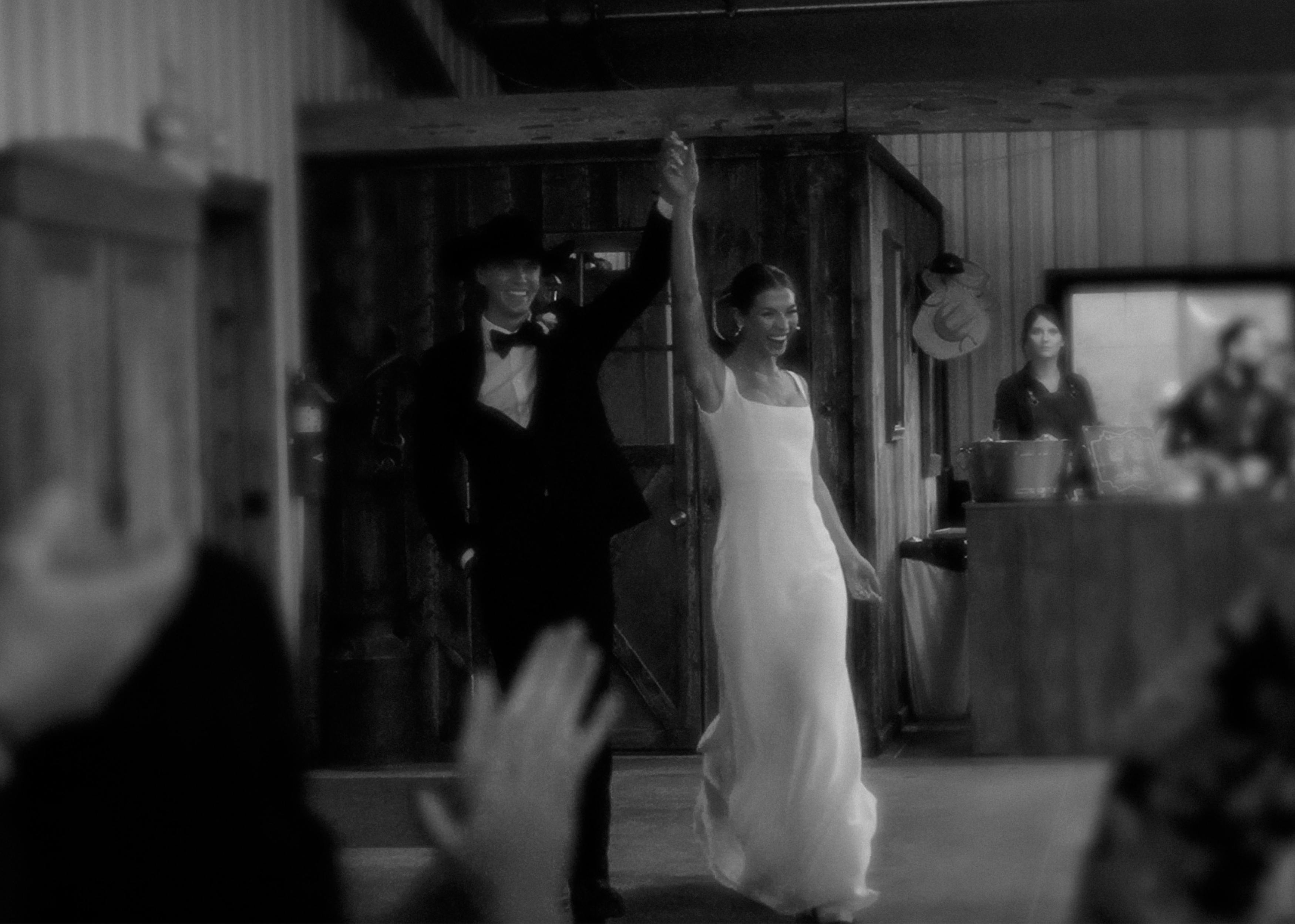 Bride and groom holding hands and raising their arms during their wedding reception, captured in a candid black-and-white moment.