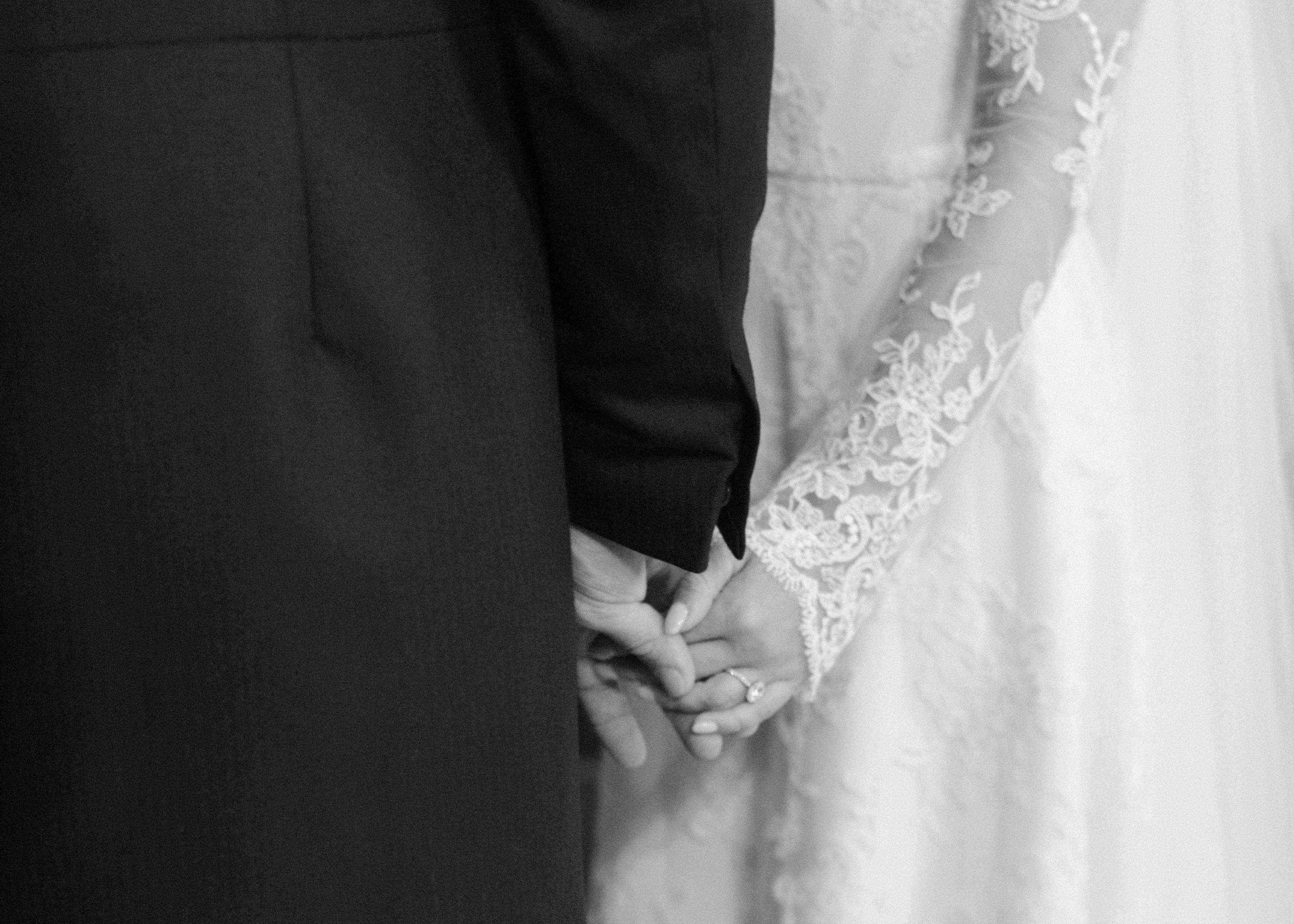 Close-up black-and-white photograph of bride and groom holding hands, highlighting the wedding rings.