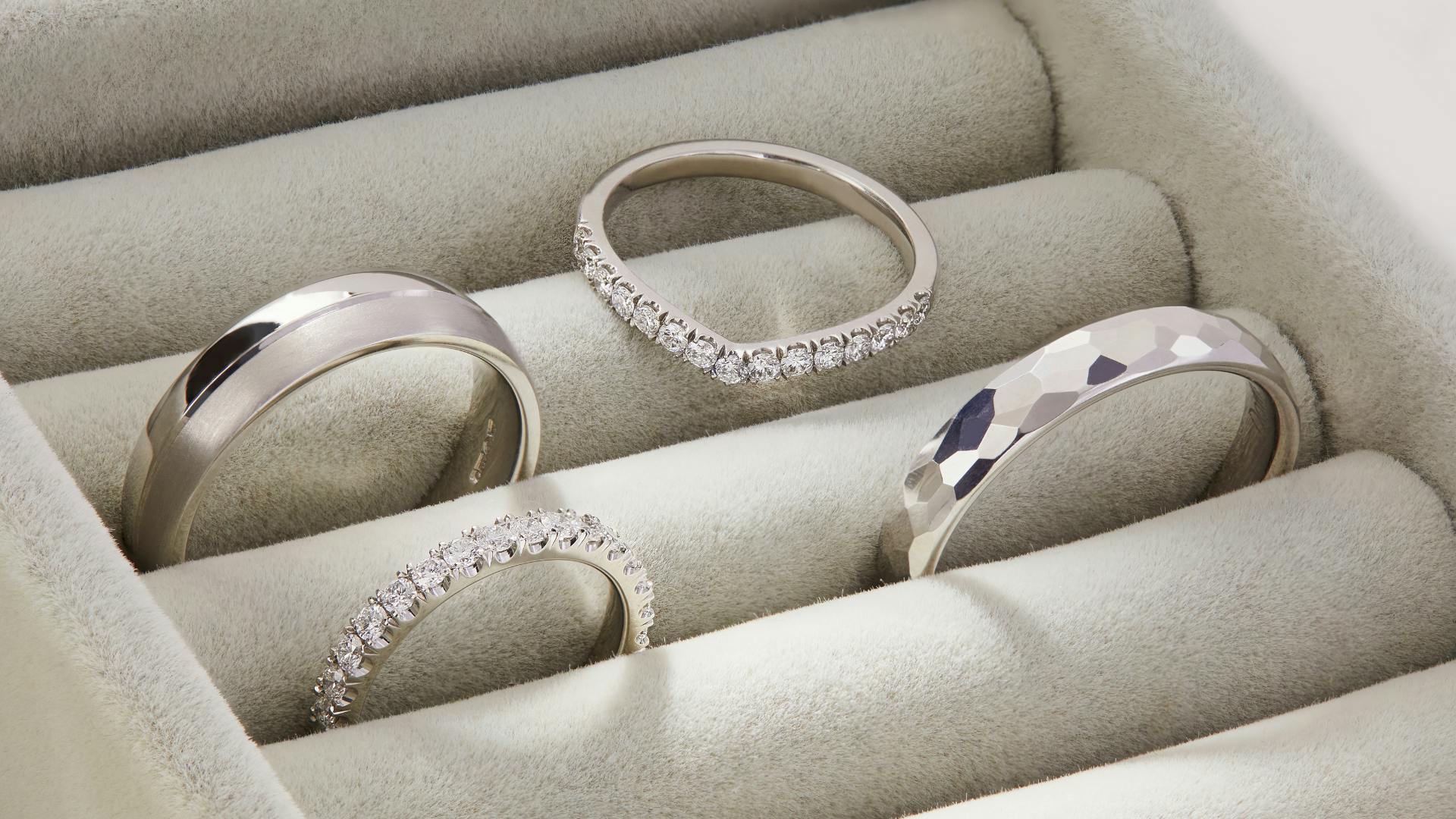 Four platinum wedding rings in ring tray, two diamond bands and two simple, textured bands.