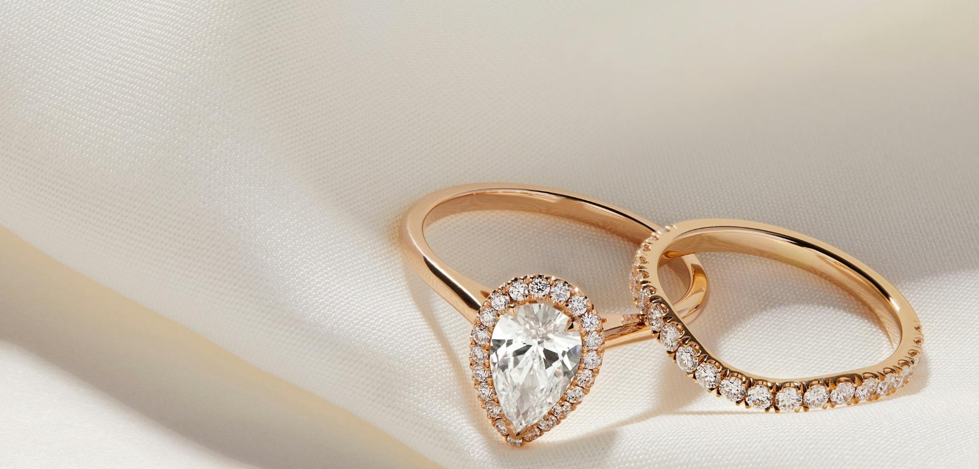 A side-view image of a rose gold halo cut diamond engagement ring set next to a curved diamond pavé wedding band.