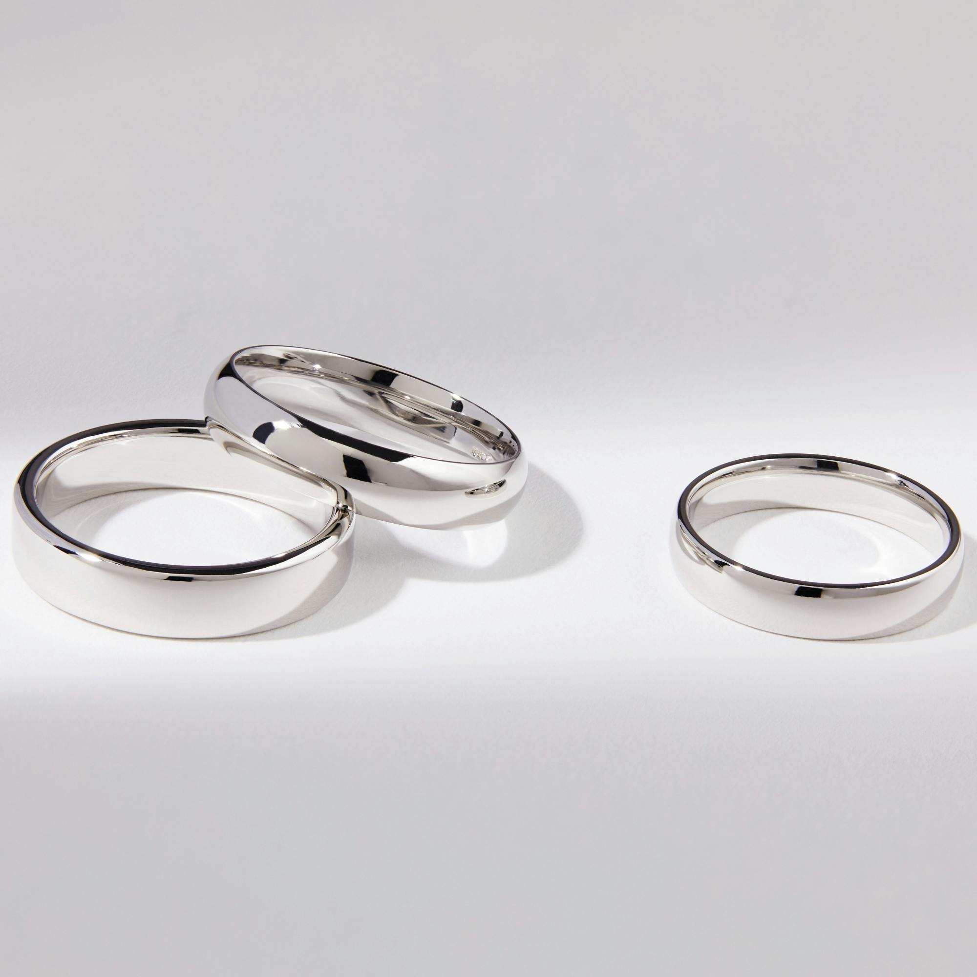 Side-view shot of three white gold wedding bands on a white, lit-up background.