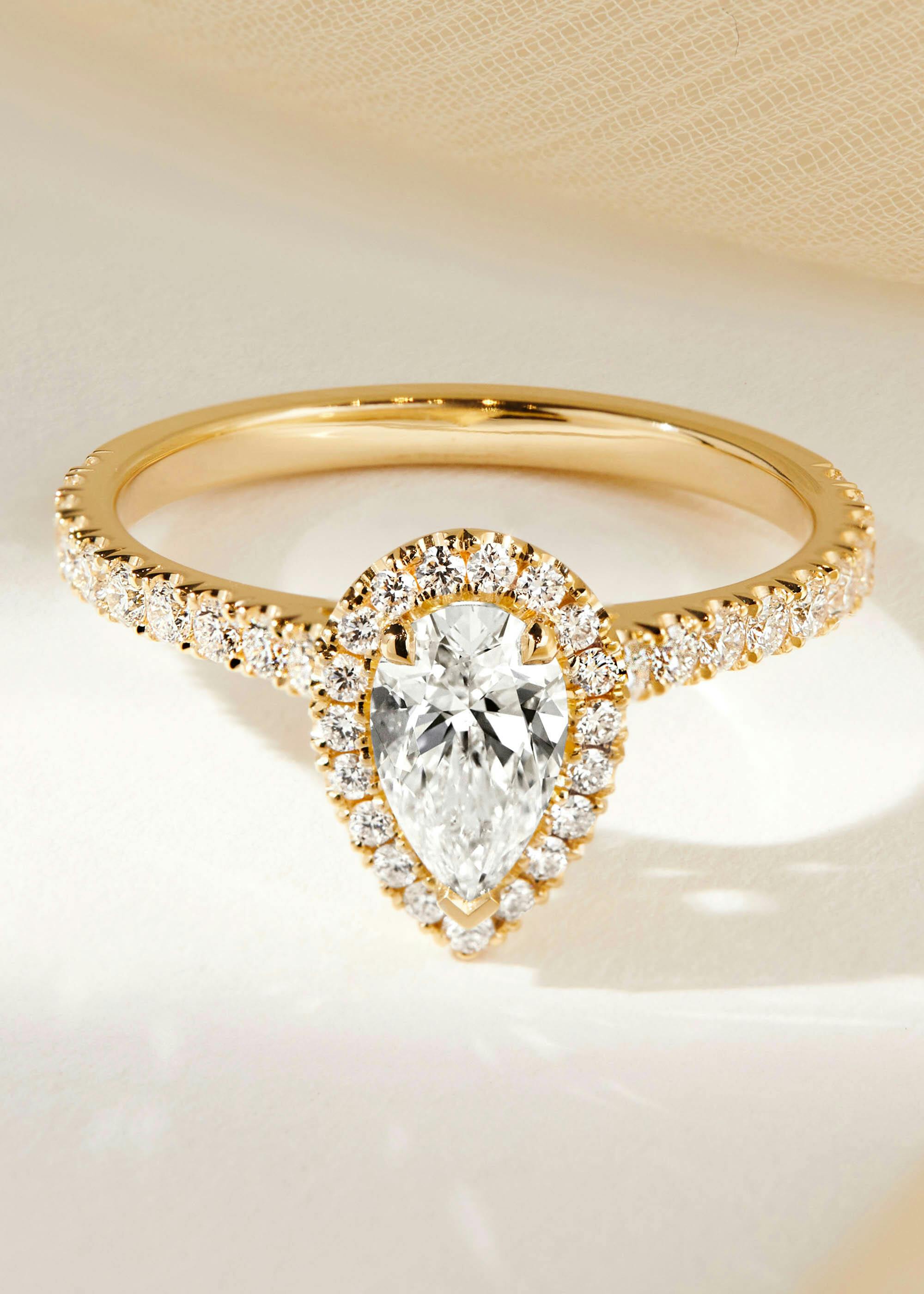 Yellow gold halo engagement ring with a pear shape diamond, white a diamond set halo and band